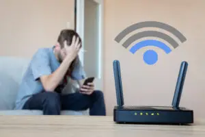 Frustrated man sitting on a couch behind a wifi router 